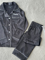 Load image into Gallery viewer, These include a button up shirt with your personalised name above the pocket and trousers, with pockets on either side and an adjustable tie around the waist. The perfect personalised gift for children! Black body colour with a White contrast piping and buttons. Personalised for you!