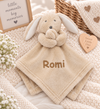A toffee plush bunny security blanket with the name 'Blake' embroidered in white script on the front, styled on a cream knit blanket with baby props.