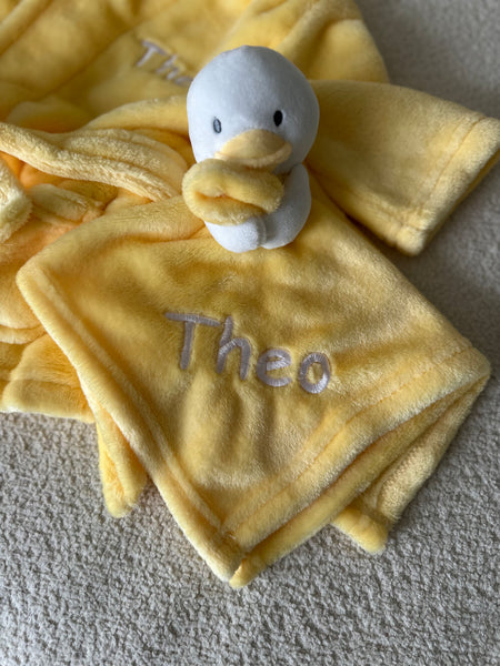 A personalised little duck comforter soft plush material in yellow, with embroidered personalised detailing set neatly across the front of the white duck.  The duck is attached with a  yellow beak and cute stitched eyes, this would make such a sweet little personalised gift. 