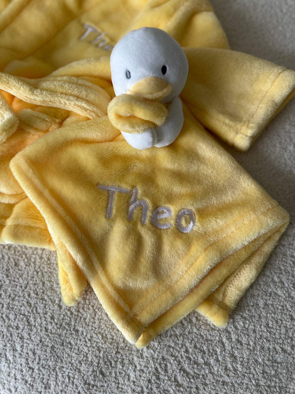 A personalised little duck comforter soft plush material in yellow, with embroidered personalised detailing set neatly across the front of the white duck.  The duck is attached with a  yellow beak and cute stitched eyes, this would make such a sweet little personalised gift. 