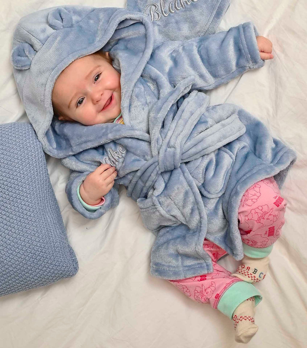  Babies personalised Dusky Blue hooded dressing gown. Made from super soft material, it features an elephant embroidery to the chest as well as detailing pom pom ears and a hood. Make it extra special by adding a personalised touch.