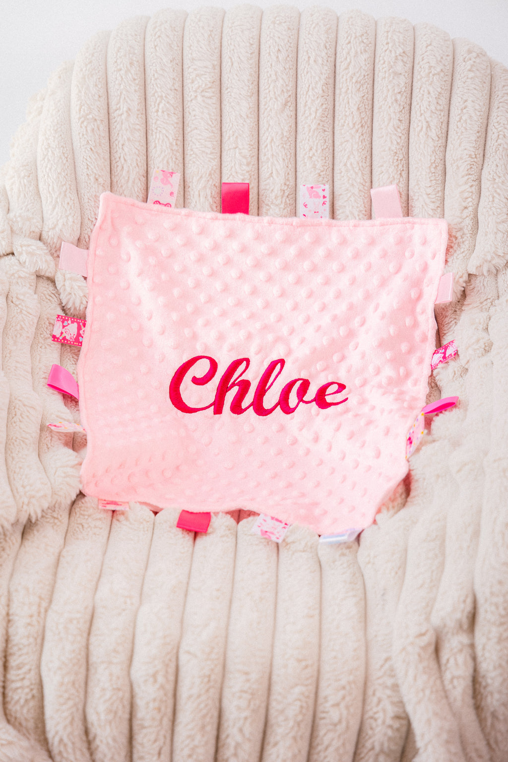 Baby girls personalised soft pink plush comforter. Personalisation embroidered in the middle in hot pink which complements the accent tags around the edges. A nice square soft comforter to help keep the little one content.