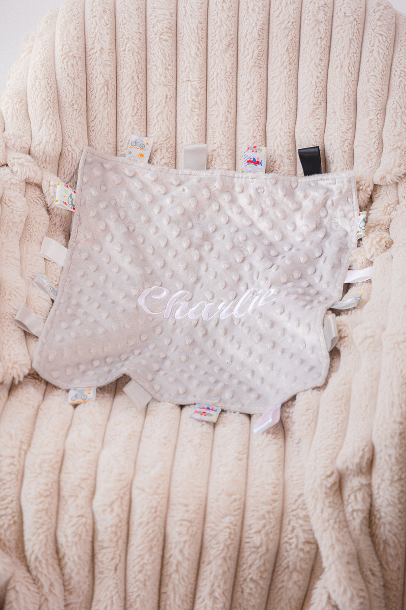 Babies unisex beige personalised soft plush comforter. Personalisation embroidered in the middle in a light beige cotton which complements the accent tags around the edges. A nice square soft comforter to help keep the little one content.
