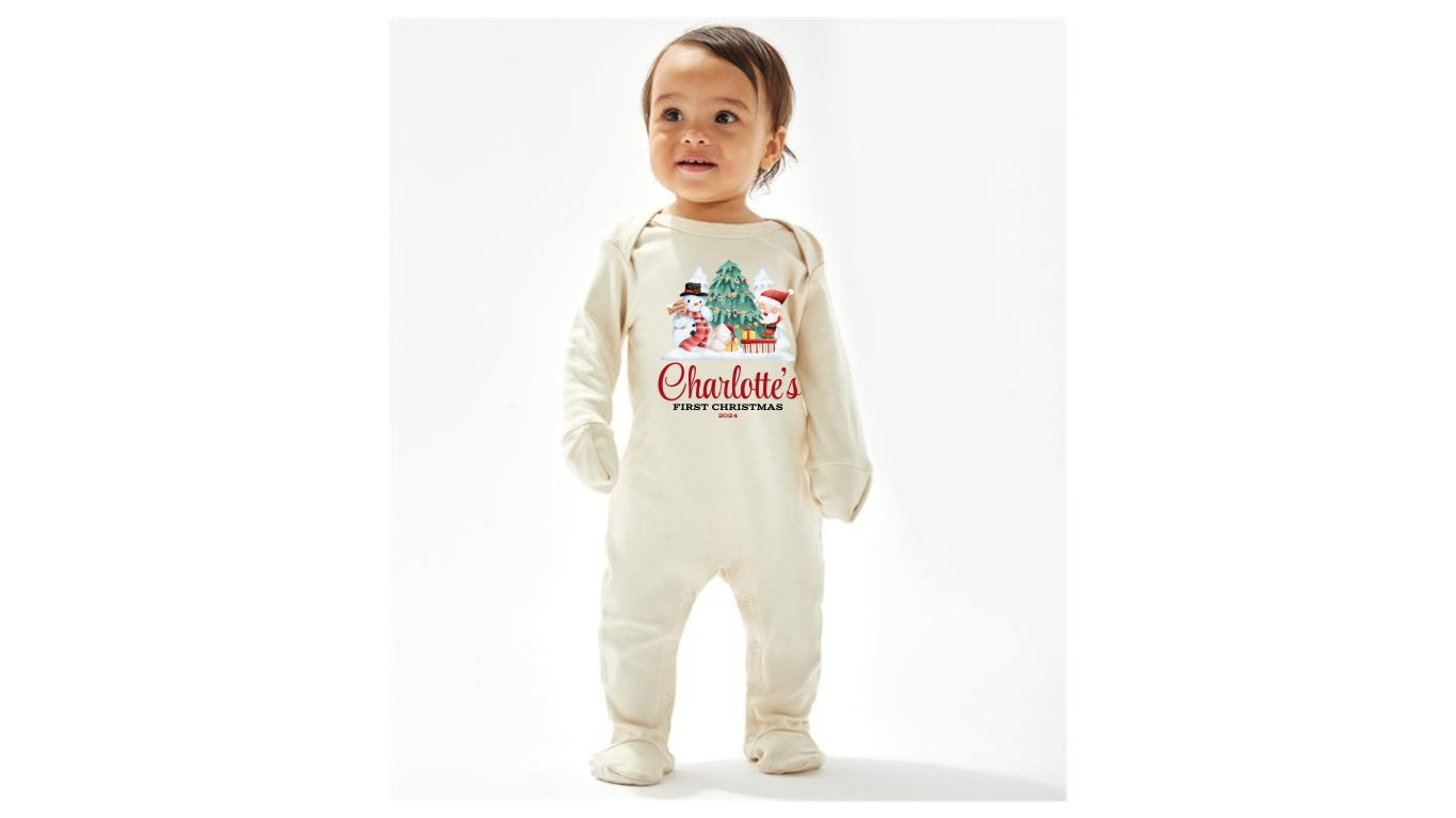 A cream personalised unisex soft cotton 
 sleep suit for babies with a Christmas theme print, including a design with Santa Claus, Christmas tree and a snowman. Personalisation to the middle below the design in red print with first Christmas written underneath. A sure way to get a first Christmas photo of your baby. 