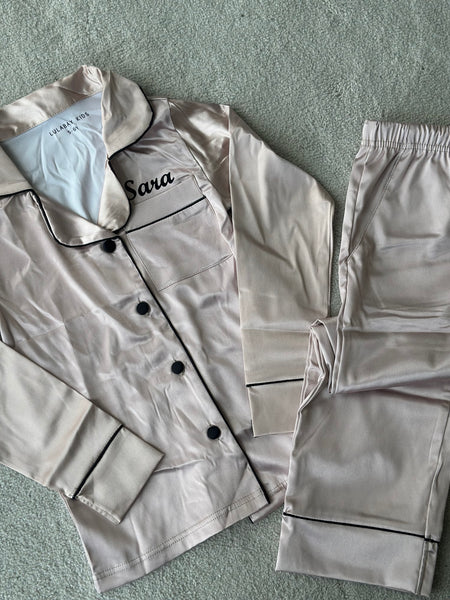 These include a button up shirt with your personalised name above the pocket and trousers, with pockets on either side and an adjustable tie around the waist. The perfect personalised gift for children! Champagne body colour with a Black contrast piping and buttons. Personalised for you! 