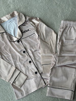 Load image into Gallery viewer, These include a button up shirt with your personalised name above the pocket and trousers, with pockets on either side and an adjustable tie around the waist. The perfect personalised gift for children! Champagne body colour with a Black contrast piping and buttons. Personalised for you! 
