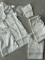 Load image into Gallery viewer, These include a button up shirt with your personalised name above the pocket and trousers, with pockets on either side and an adjustable tie around the waist. The perfect personalised gift for children! Ivory body colour with a Champagne contrast piping and buttons. Personalised for you! 
