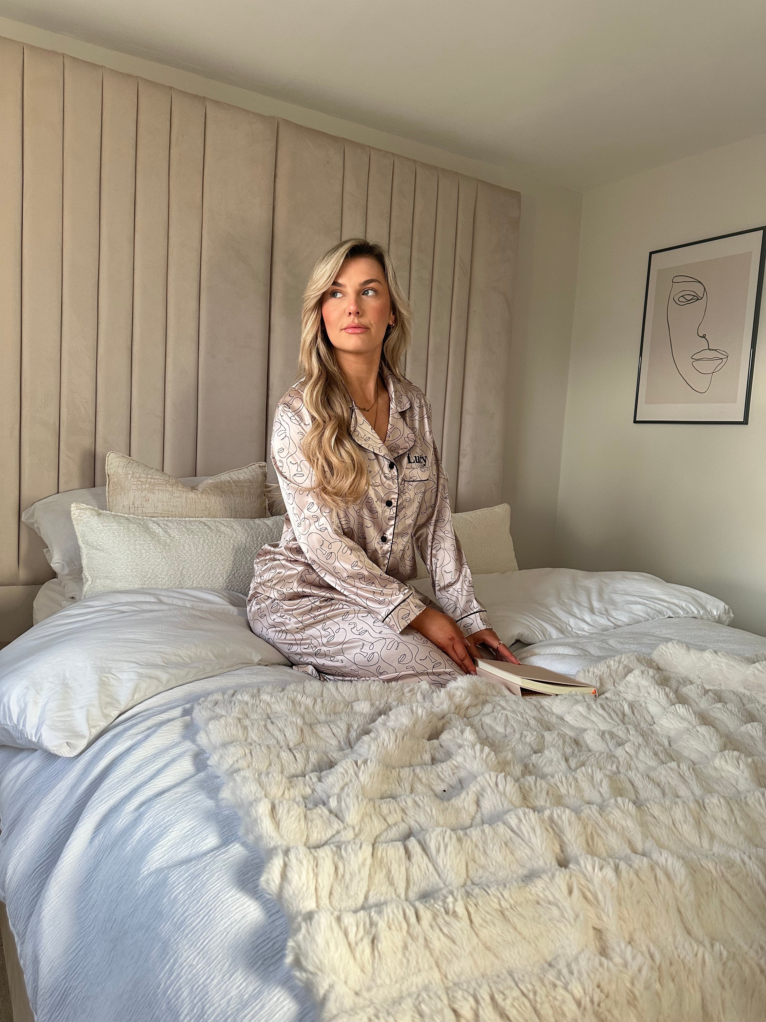 Ladies personalised satin pyjamas featuring a long sleeve shirt, button up design and pocket to the right of the shirt with personalisation above the pocket. Matched with trousers with pockets on either side and adjustable drawcord around the waist. Both the shirt and trouser in this pyjama set is sold as a set together, with a luxurious abstract face design all over and contrast piping. 