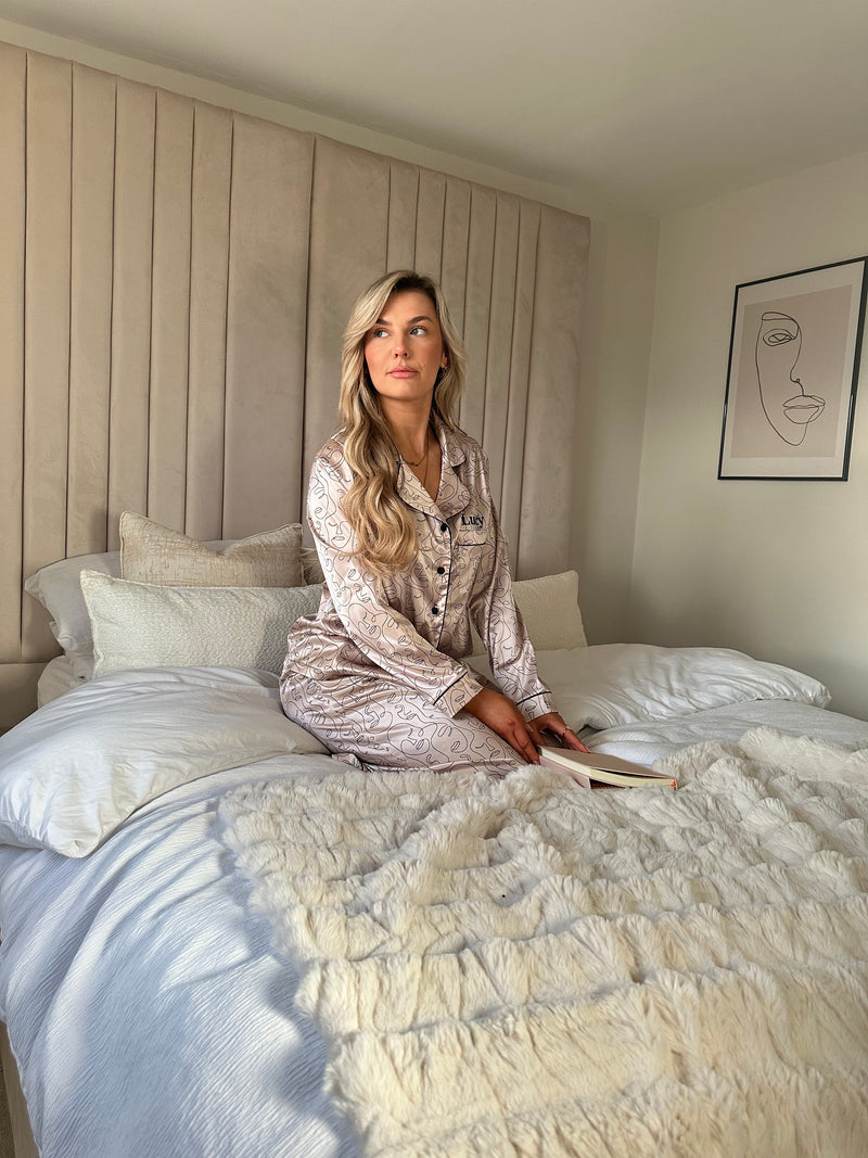 Ladies personalised satin pyjamas featuring a long sleeve shirt, button up design and pocket to the right of the shirt with personalisation above the pocket. Matched with trousers with pockets on either side and adjustable drawcord around the waist. Both the shirt and trouser in this pyjama set is sold as a set together, with a luxurious abstract face design all over and contrast piping. 