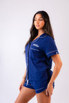 Ladies short jersey pyjamas in Navy with a White contrast satin piping and buttons. Short sleeve button shirt with a pocket to the right of the chest and your personalised name above. Shorts with both pockets and an adjustable tie around the waist. 