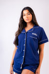 Ladies short jersey pyjamas in Navy with a White contrast satin piping and buttons. Short sleeve button shirt with a pocket to the right of the chest and your personalised name above. Shorts with both pockets and an adjustable tie around the waist. 