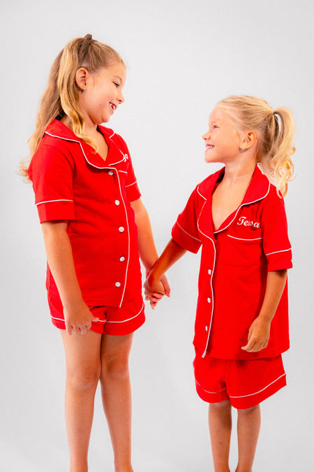 Ladies short jersey pyjamas in Red with a White contrast satin piping and buttons. Short sleeve button shirt with a pocket to the right of the chest and your personalised name above. Shorts with both pockets and an adjustable tie around the waist. 