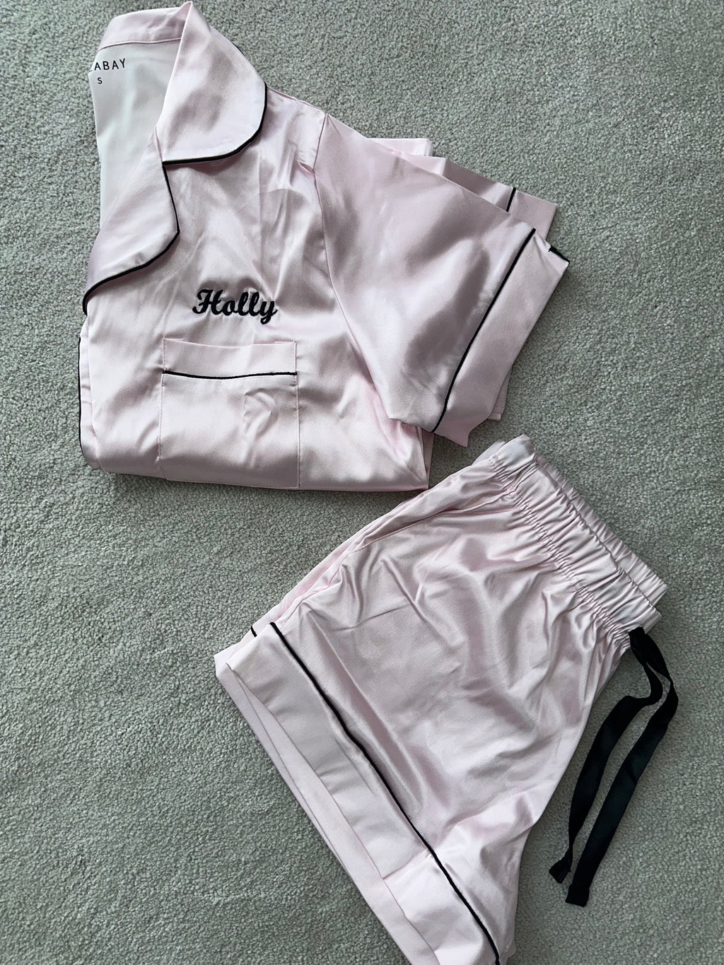 Ladies light pink satin pyjamas. Button up shirt with your personalised name above the pocket with matching shorts. Body colour light pink with a black contrast piping and buttons. Personalised for you! 