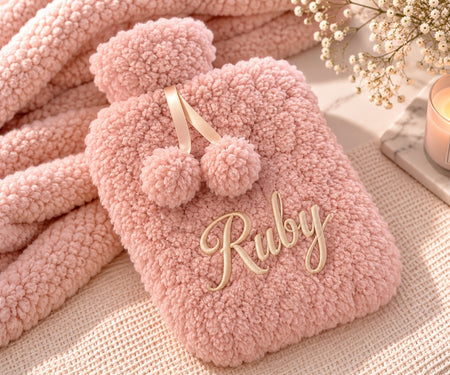 Personalised hot water bottle in a Dusky Pink colour. Created from a premium borg fabric with a name embroidered on the front cover of the hot water botttle and a rubber insert of 2L inside. 